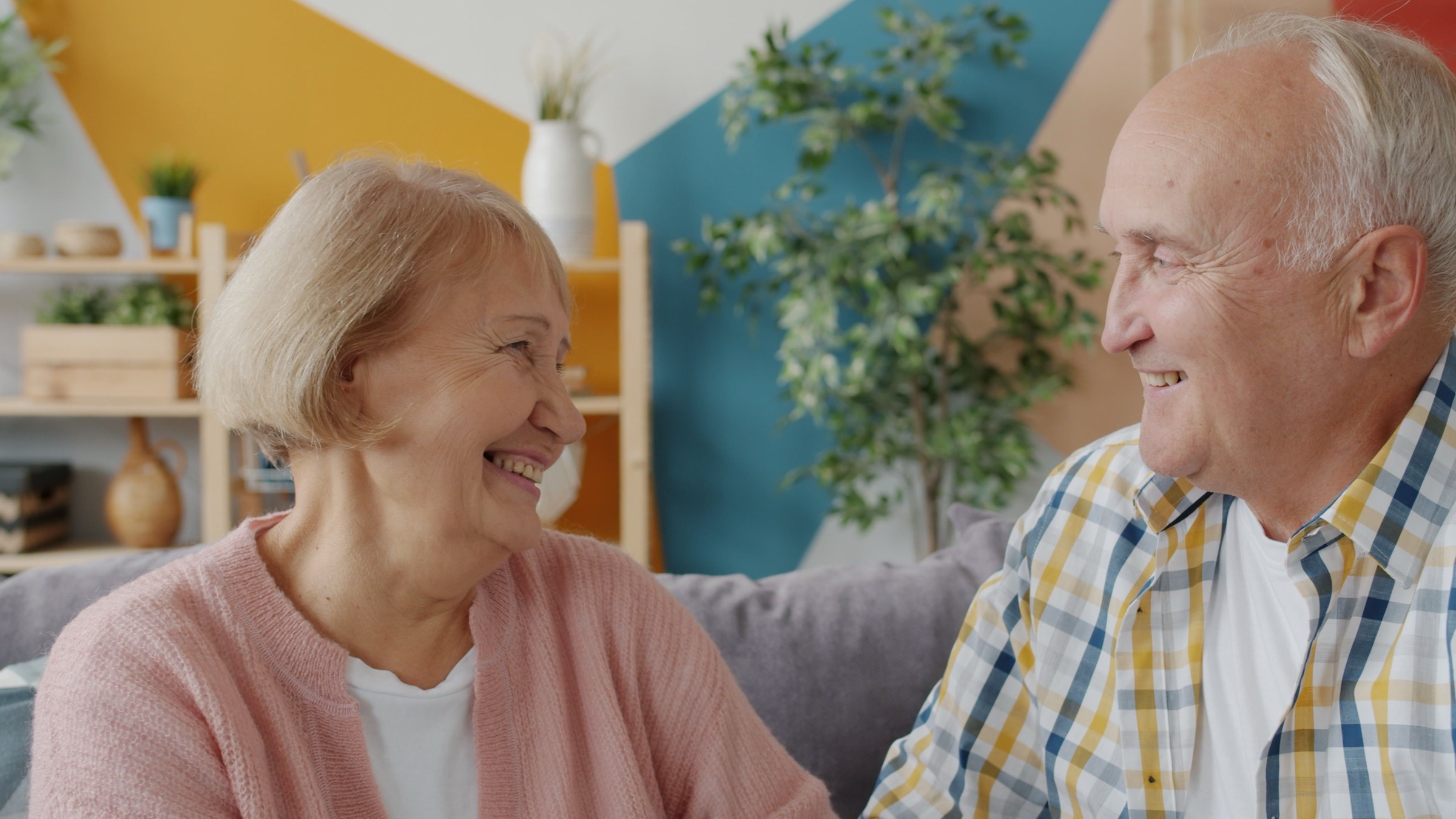 An older couple sitting together on the sofa in their living room, laughing.
