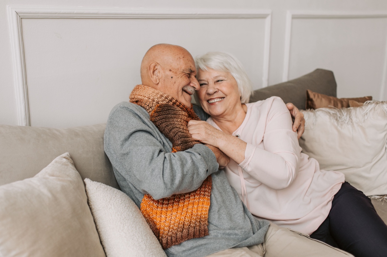 An older couple laughing together on the sofa at home