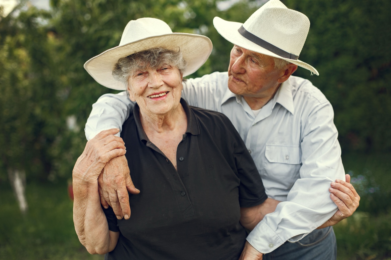 A smiling older couple in sun hats, arm in arm in their garden