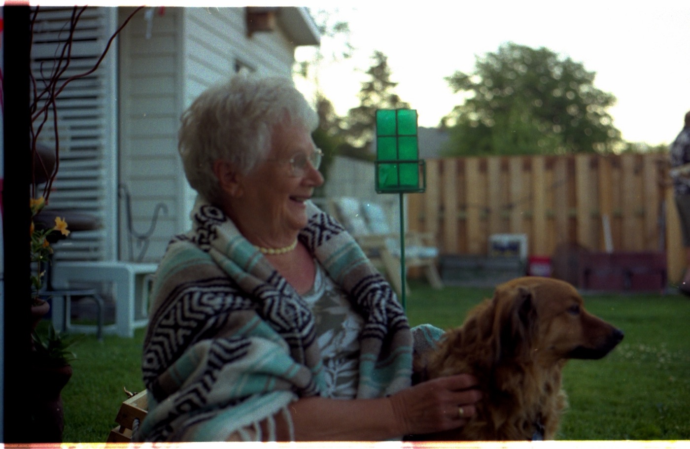 A smiling older woman sitting in her garden with her dog