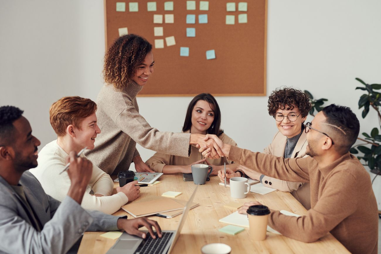 A team meeting around a table, two colleagues shaking hands